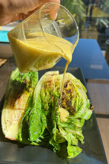 Liquid Gold Tahini Dressing being drizzled over a bed of grilled romaine lettuce.