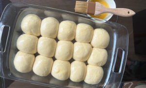 Rolls of dough in baking dish brushed with egg wash.