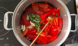 Fresno Chilies, rosemary, garlic, and a bay leaf simmering in a pot of boiling salted water.